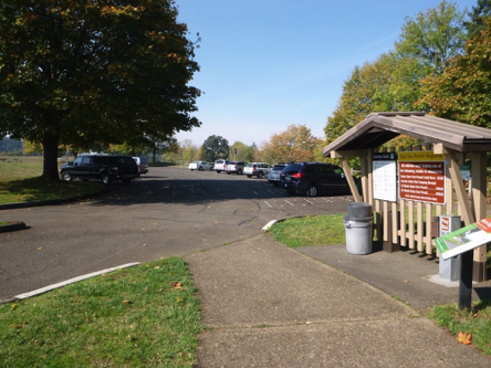 Parking lot &ndash; picnic benches in grassy area &ndash; informational kiosk &ndash; curb-cut leading to the visitor center