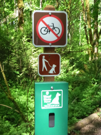 Sign at natural surface trail: No bikes, dogs on leashes only and dog waste bag container Sign at natural surface trail: No bikes, dogs on leashes only and dog waste bag container